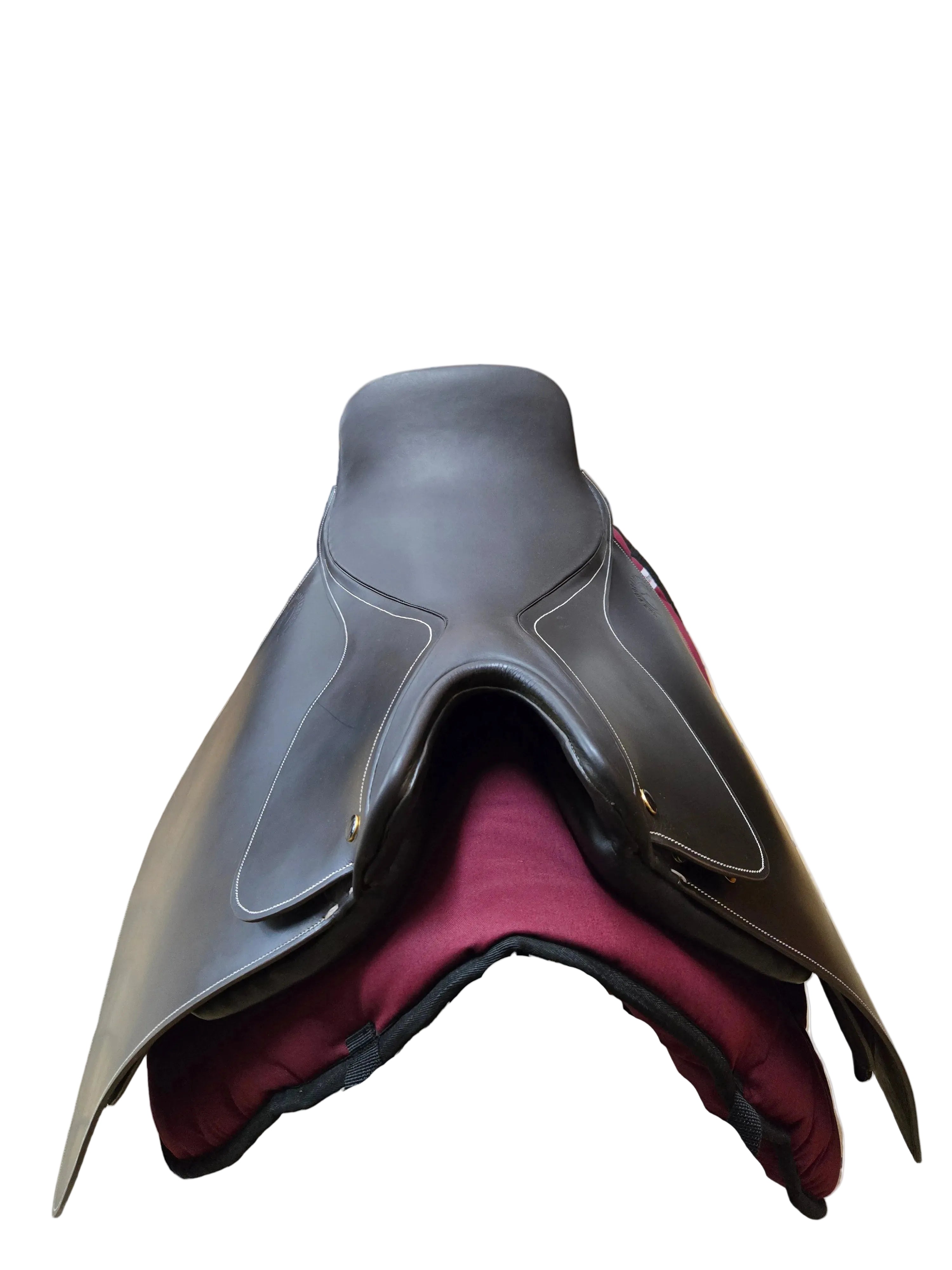 A dark brown leather equestrian saddle with white contrast stitching, displayed on a black stand with a burgundy saddle pad inside what appears to be a showroom or stable.